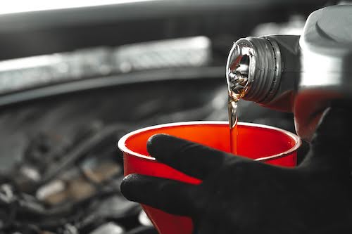 close up of auto mechanic pouring motor oil into a red funnel